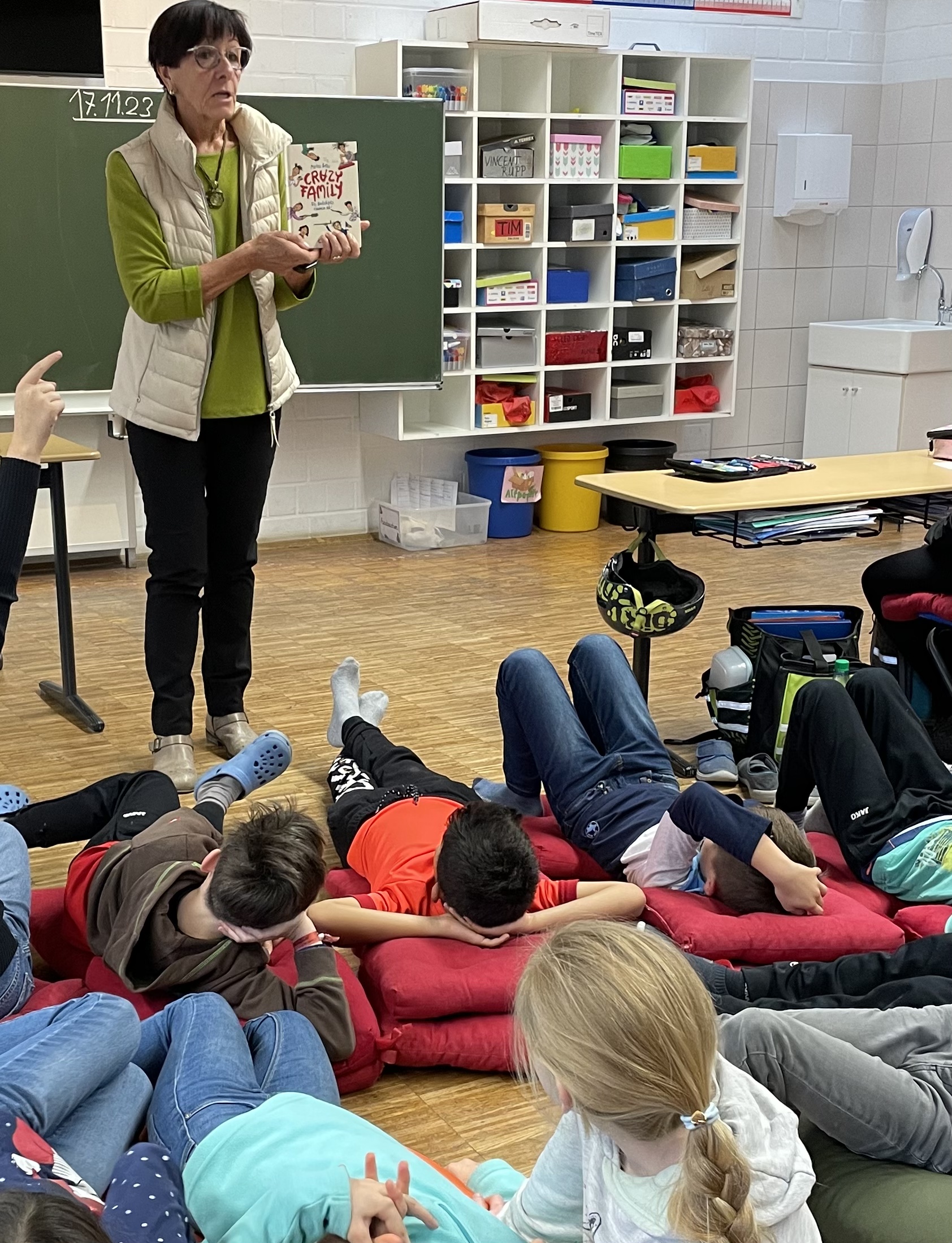 Eine Lehrerin zeigt mit ausgestreckter Hand den Kindern ein Buch